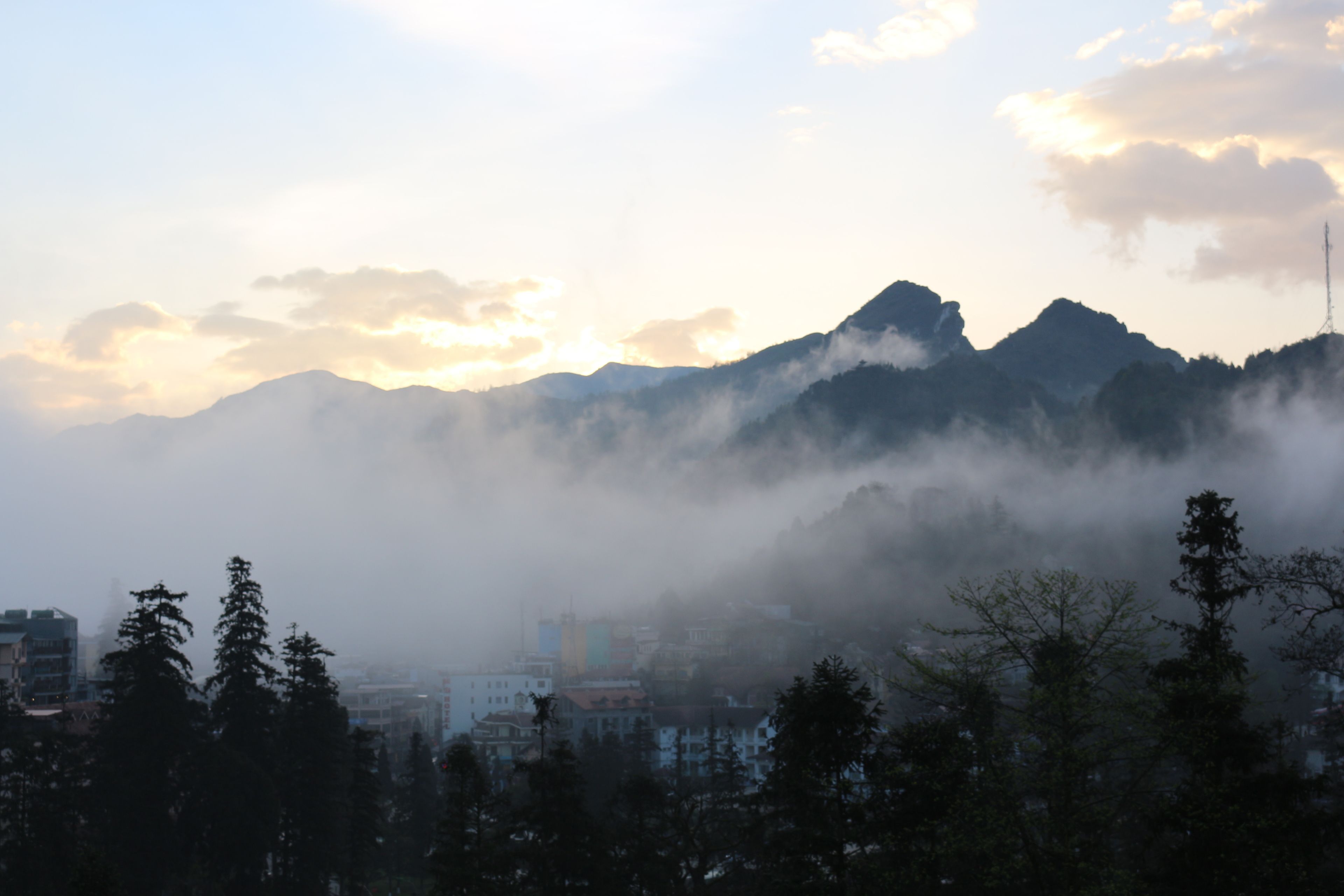 A mountainous landscape with a city in the foreground, featuring buildings and trees.