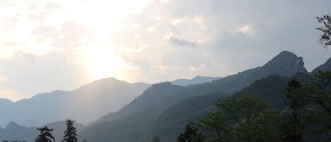 A mountainous landscape with a view of the sun setting or rising behind the hills.