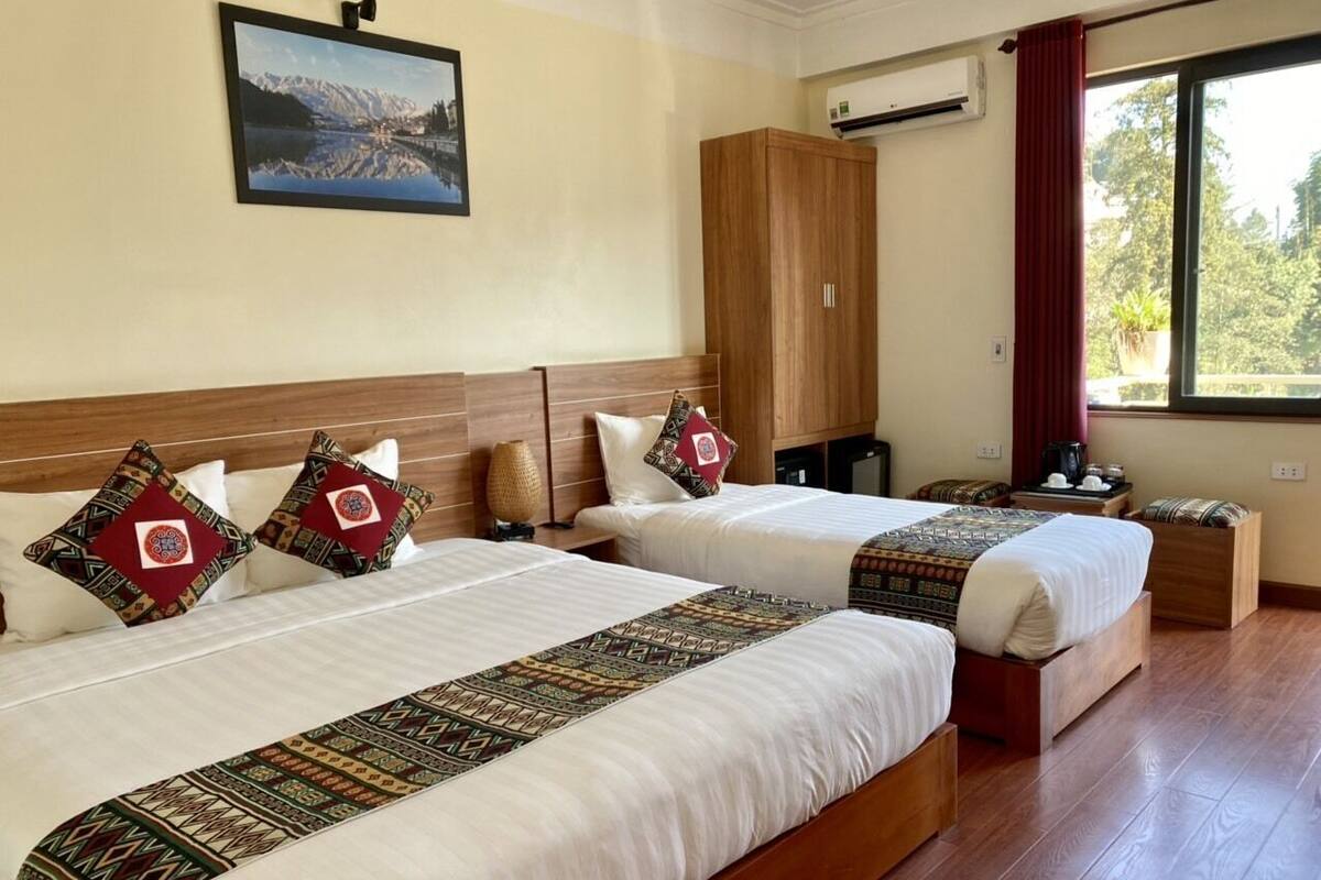 Ett hotellrum med två sängar, en garderob i trä, ett fönster med utsikt och en tavla som hänger på väggen.