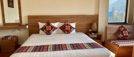 A hotel room with a large bed, a bedside table, a nightstand, a window with a view, and a wall-mounted picture.