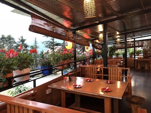 A restaurant with wooden tables and benches, potted plants, and a view of trees and flowers outside. - Sapa Garden Hotel (Sa Pa)