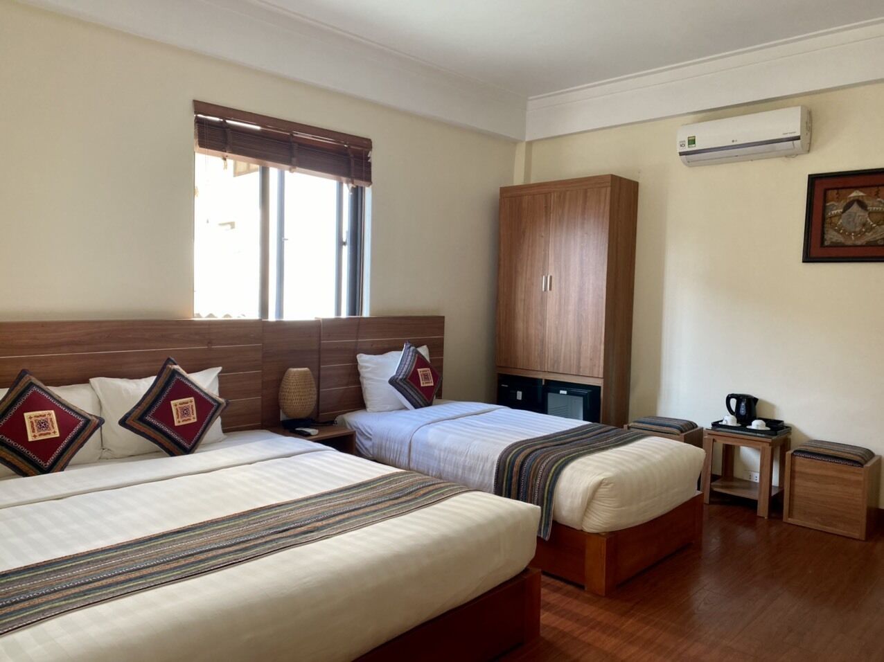 Ein Hotelzimmer mit zwei Betten, einem Holzschrank, einem kleinen Tisch mit Kaffeemaschine und einer Wandgeräteluftanlage.