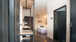Una habitación de hotel moderna con una cama, un escritorio con una silla, un espejo y una puerta con un persiano negro.
