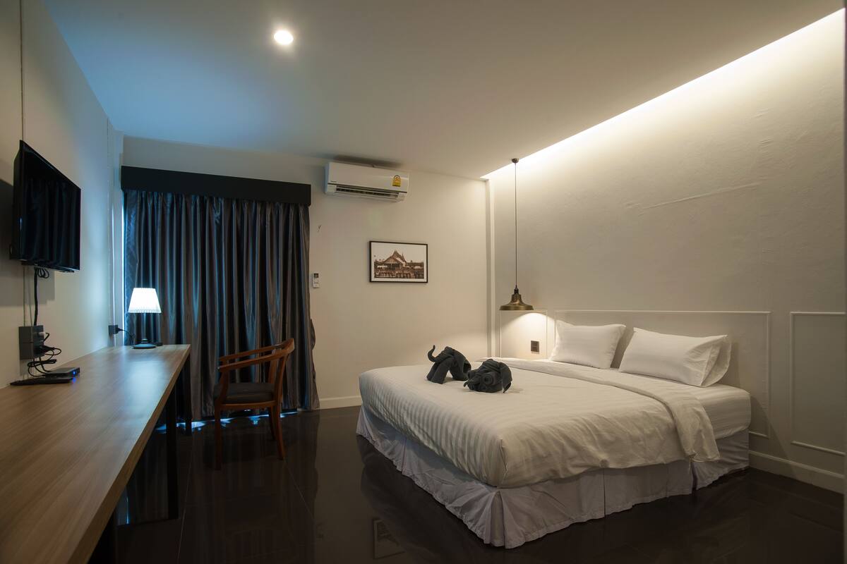 Una habitación de hotel con una cama, un escritorio, una silla, un televisor, aire acondicionado y una lámpara.