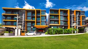 A modern multi-story hotel with balconies, a covered entrance, and a white car parked in front. - Aspira Residences Samui (Koh Samui)