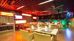 A restaurant with wicker furniture, a TV screen, and a pool area. - Aspira Residences Samui (Koh Samui)