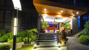 A modern hotel entrance with a staircase leading to a covered area, outdoor lighting, and a decorative water feature. - Aspira Residences Samui (Koh Samui)