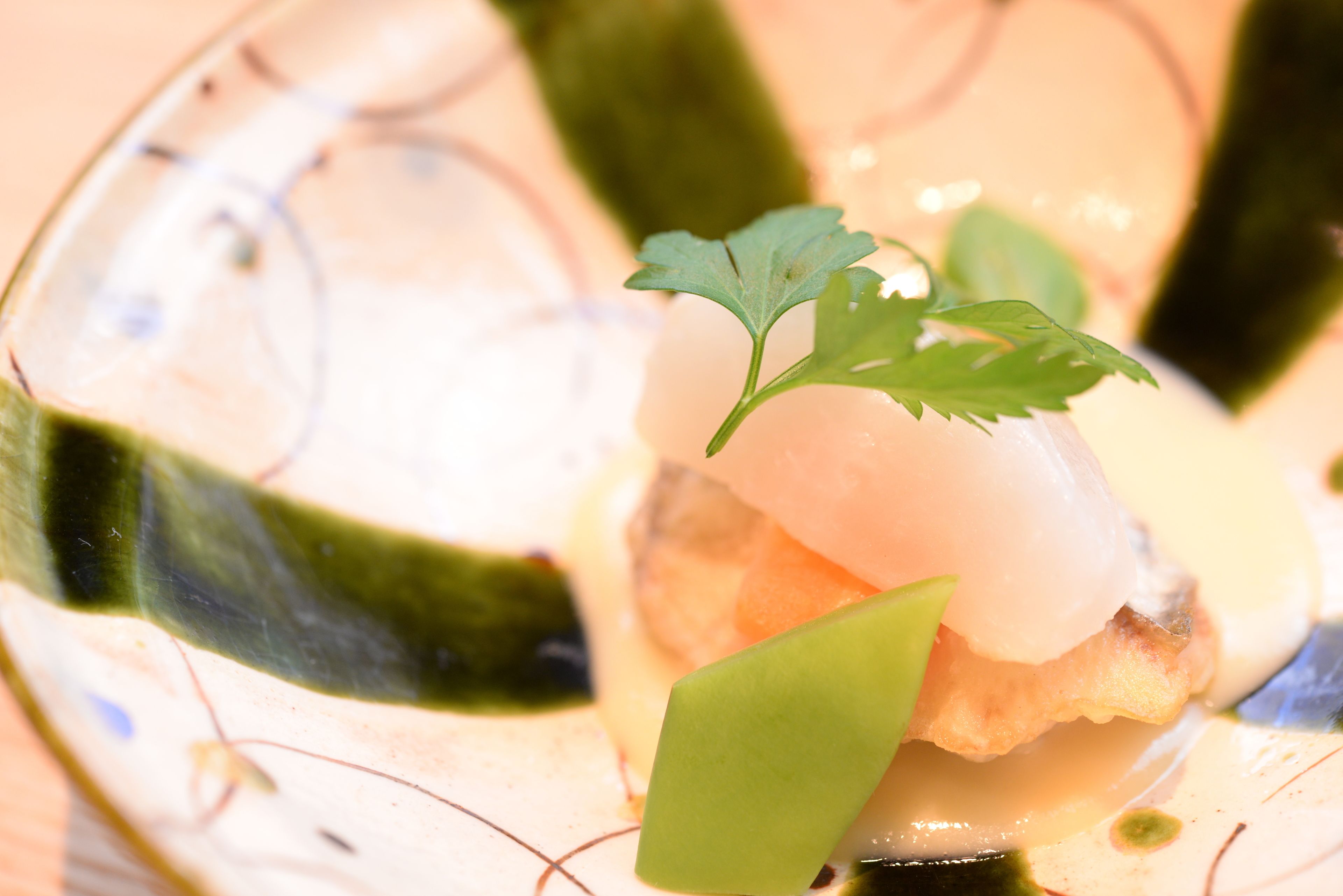 Une vue rapprochée d’une assiette contenant des sushis, des feuilles vertes et une sauce.