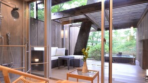 Un spa moderno con cabina de ducha de vidrio, zona de estar con sofá y mesa, y vistas a un jacuzzi y vegetación exterior.