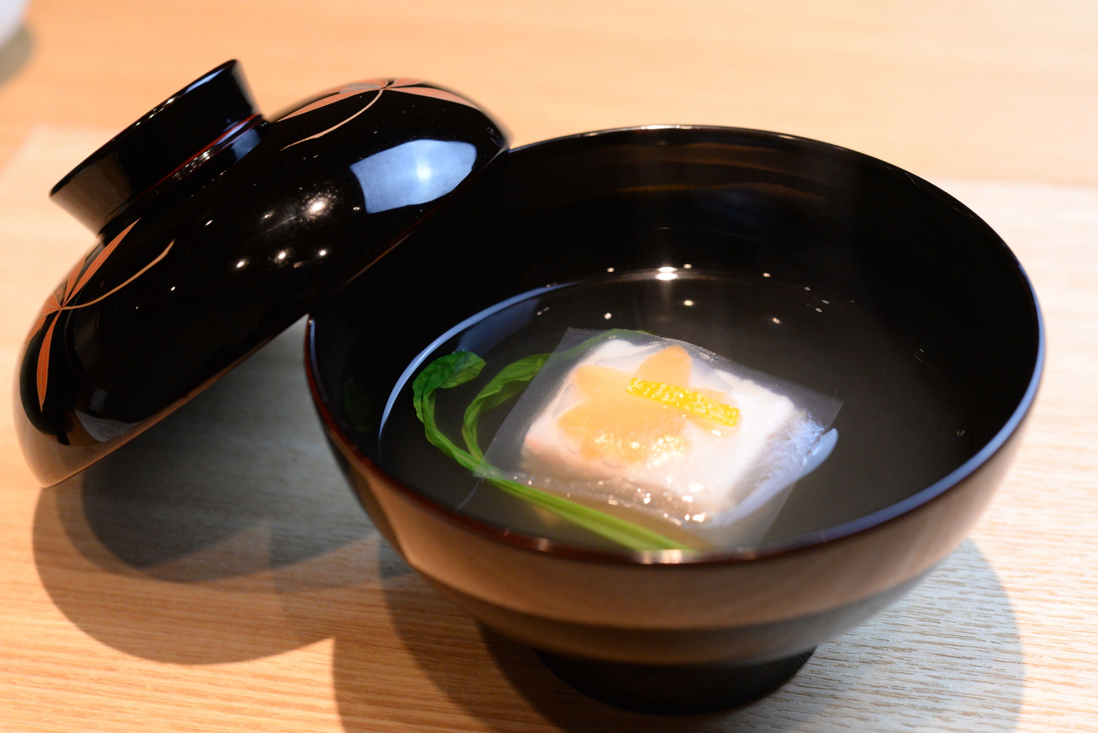 A black bowl with a lid, containing a clear liquid and a white cube.