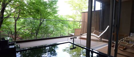A serene indoor pool with a wooden deck and lounge chairs, surrounded by lush greenery.
