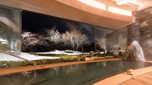 Una piscina interior moderna con pared de vidrio, pared de piedra y vista a un paisaje nevado.