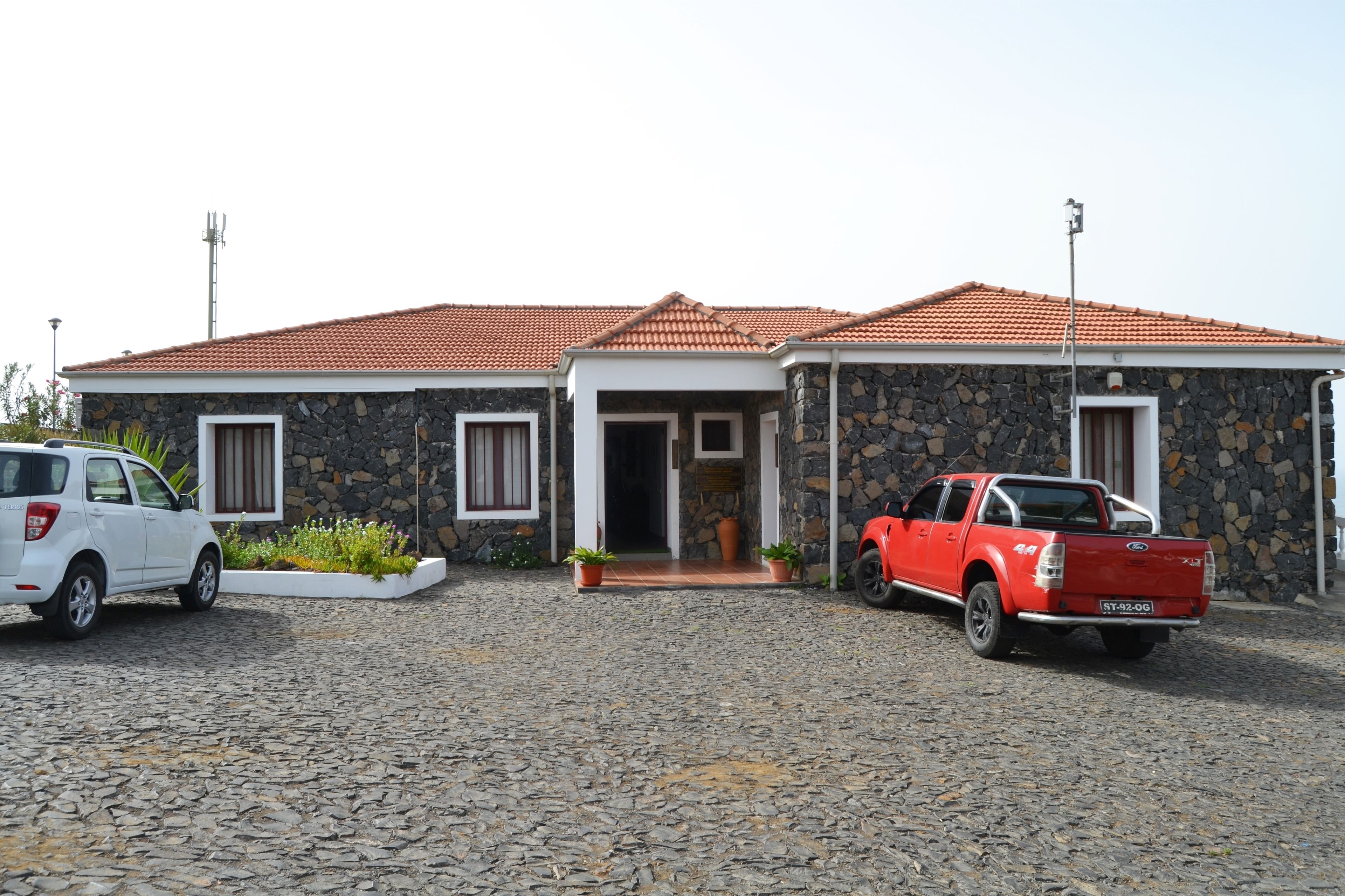 A stone house with a tiled roof, a driveway, and two parked vehicles.