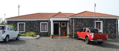 A stone house with a tiled roof, a driveway, and two parked vehicles.