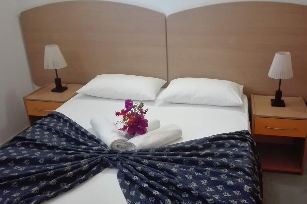 Una cama bien hecha con sábanas blancas, dos lámparas de noche y un arreglo floral sobre los almohadones.