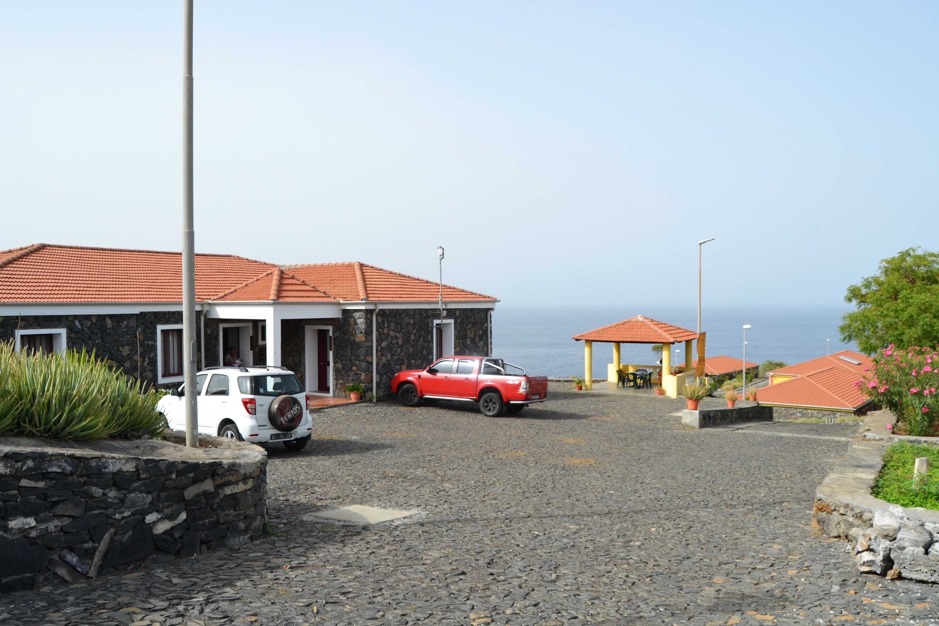A building with a stone facade and red-tiled roof, a white car, and a red car parked in front.