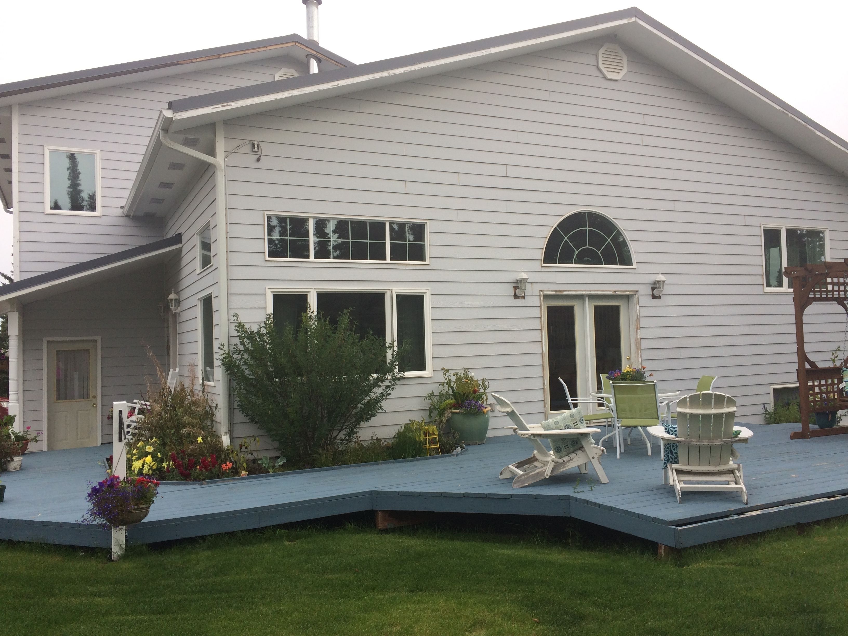 A two-story house with a covered porch, a small garden, and outdoor furniture.