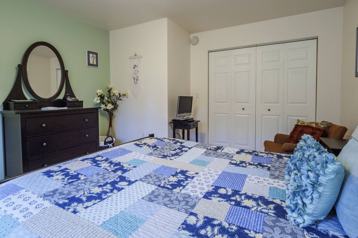 A bedroom with a large bed, a dresser, a mirror, a desk, a chair, and a wardrobe.