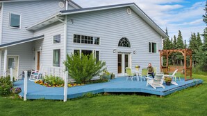 Una casa de dos pisos con un balcón azul, fachada blanca y una pérgola de madera.