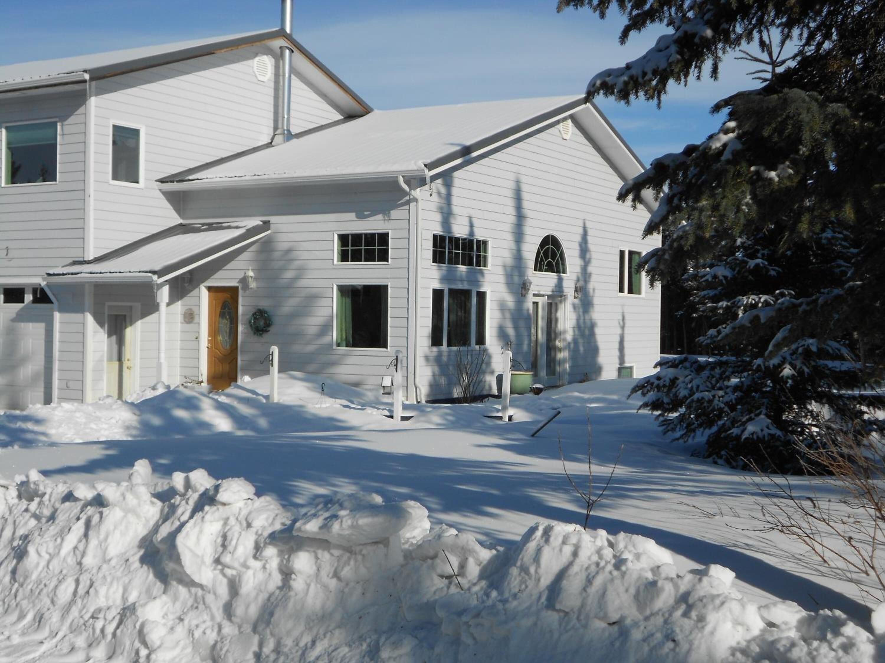 A two-story white house with a snow-covered driveway and a large snowbank in front.