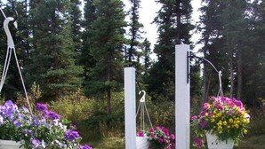 Un jardín con terraza de madera, rodeado de abundante vegetación y cestas de flores colgantes.