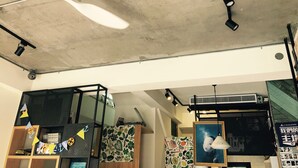 Una habitación con ventilador de techo, luces empotradas, un estante de madera con juguetes, un papel tapiz estampado y un cuadro enmarcado.