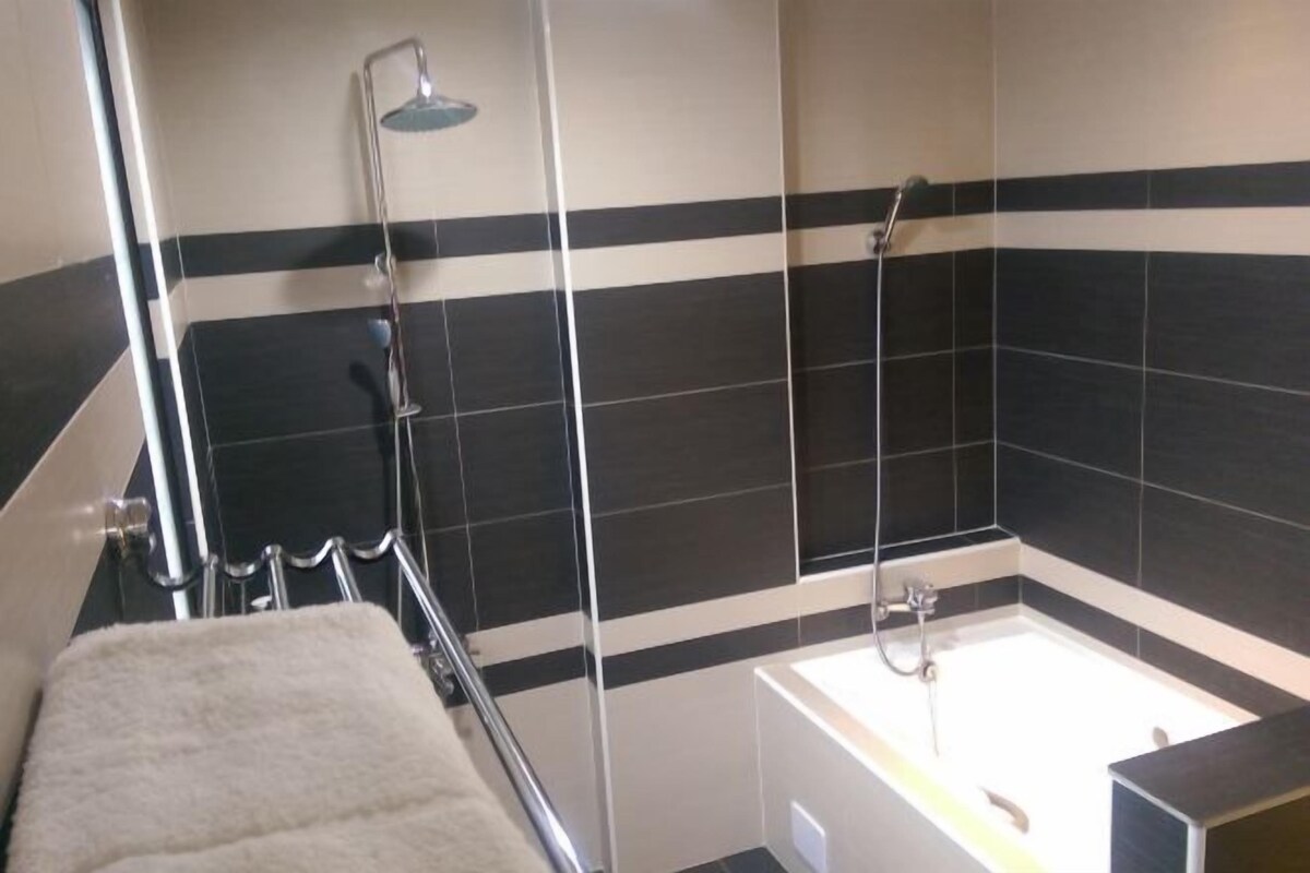 A modern bathroom with a bathtub, shower, and towel rack.