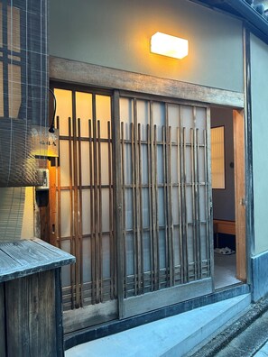 A traditional Japanese entrance with a sliding wooden gate, a small wooden table, and a wall-mounted light fixture.