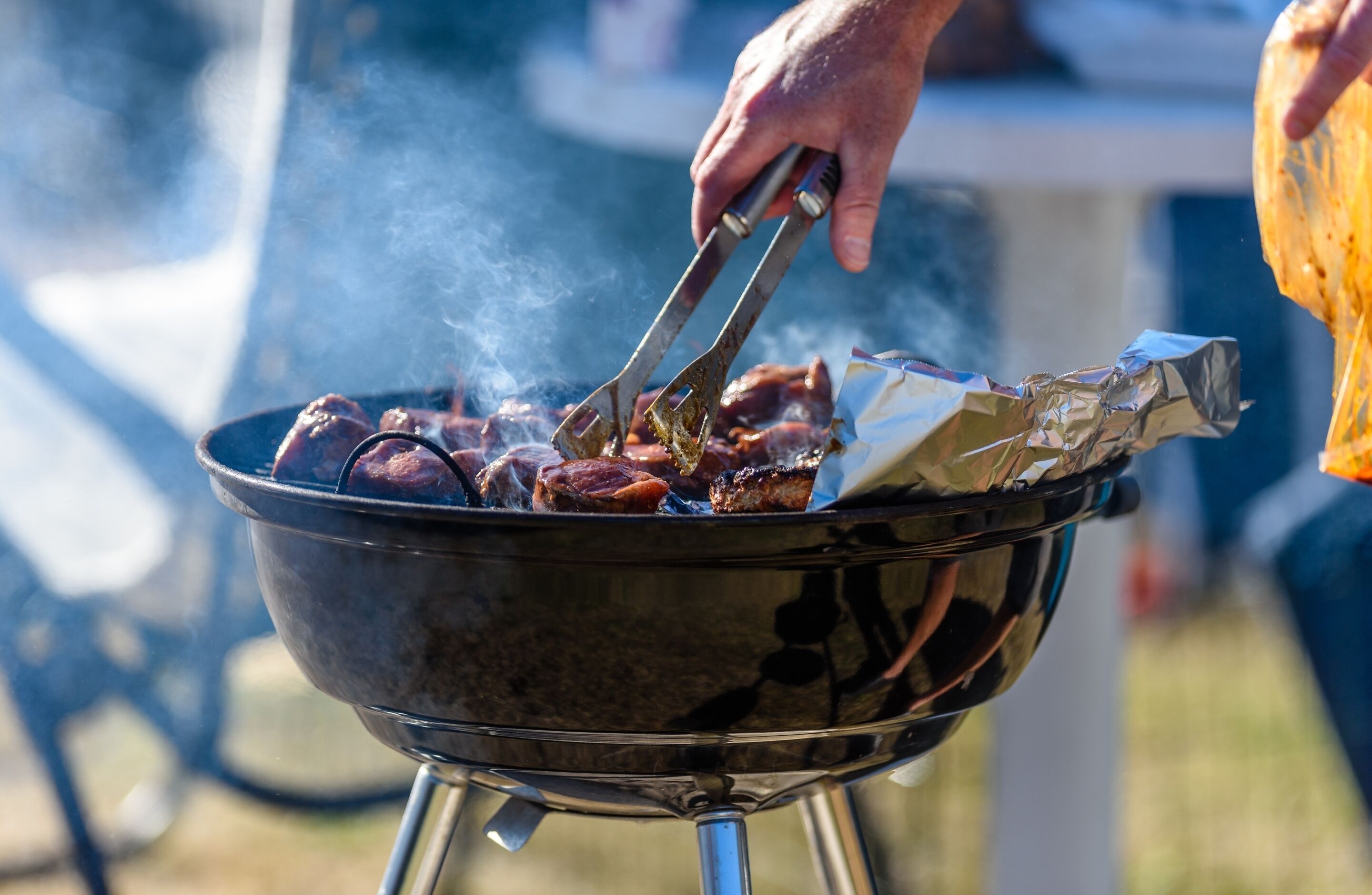 A person grilling meat on an outdoor barbecue.