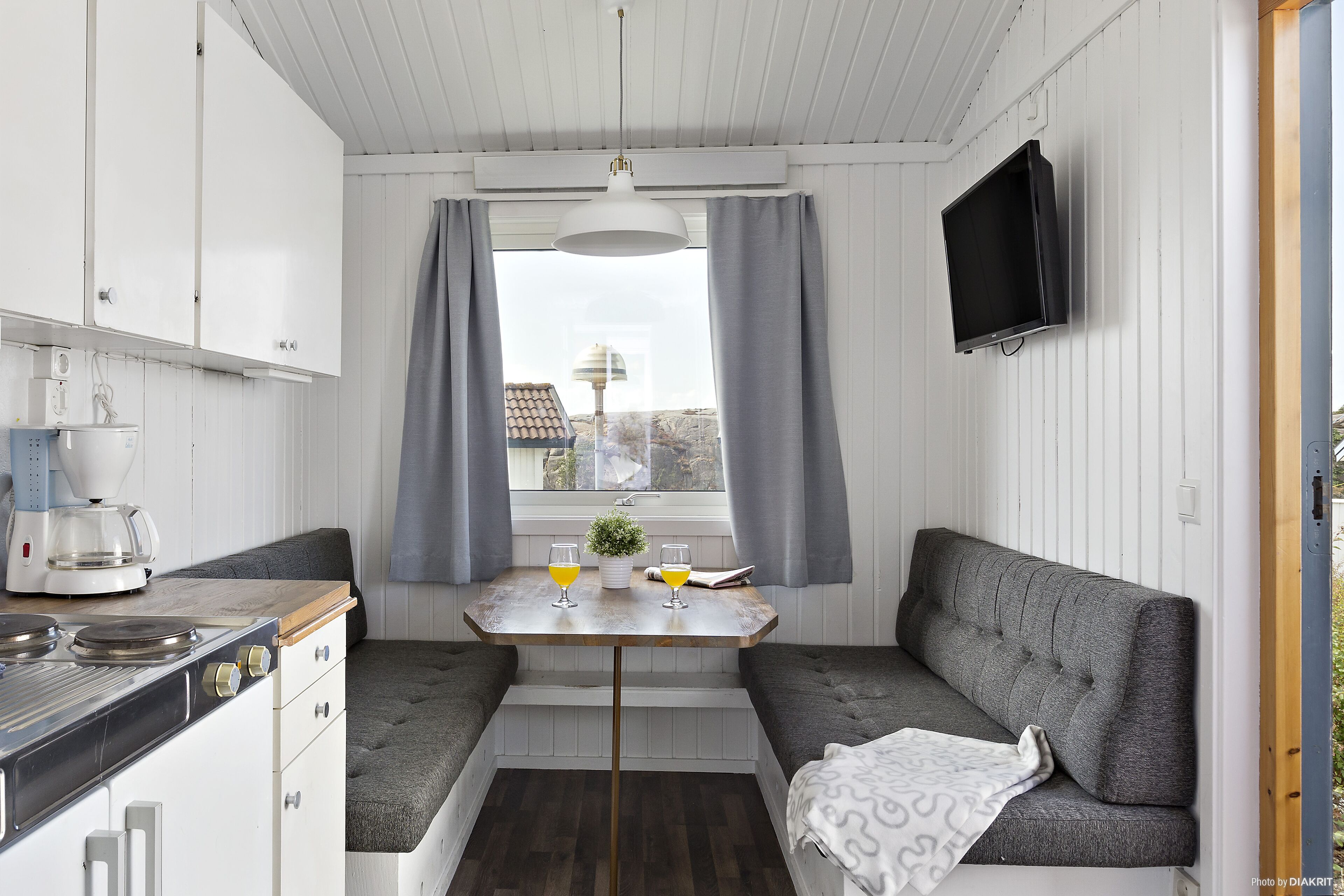 A compact kitchen with a stove, a table with two glasses of orange juice, and a grey sofa.