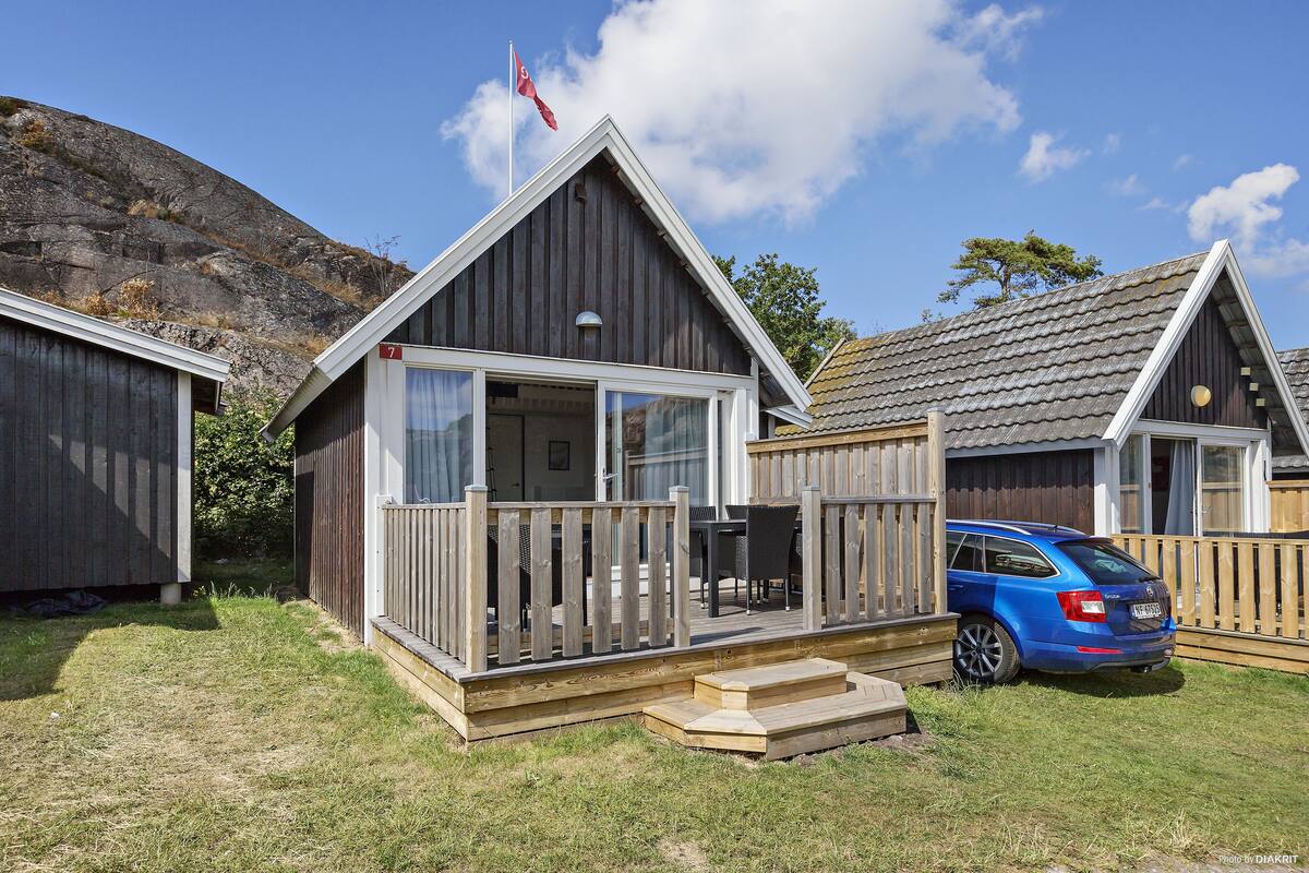 A small cabin with a deck, a car parked in front, and a flag on top.