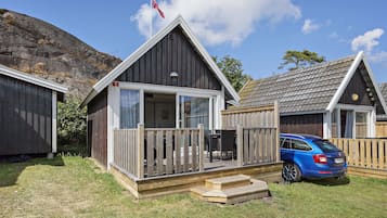 A small cabin with a deck, a car parked in front, and a flag on top.