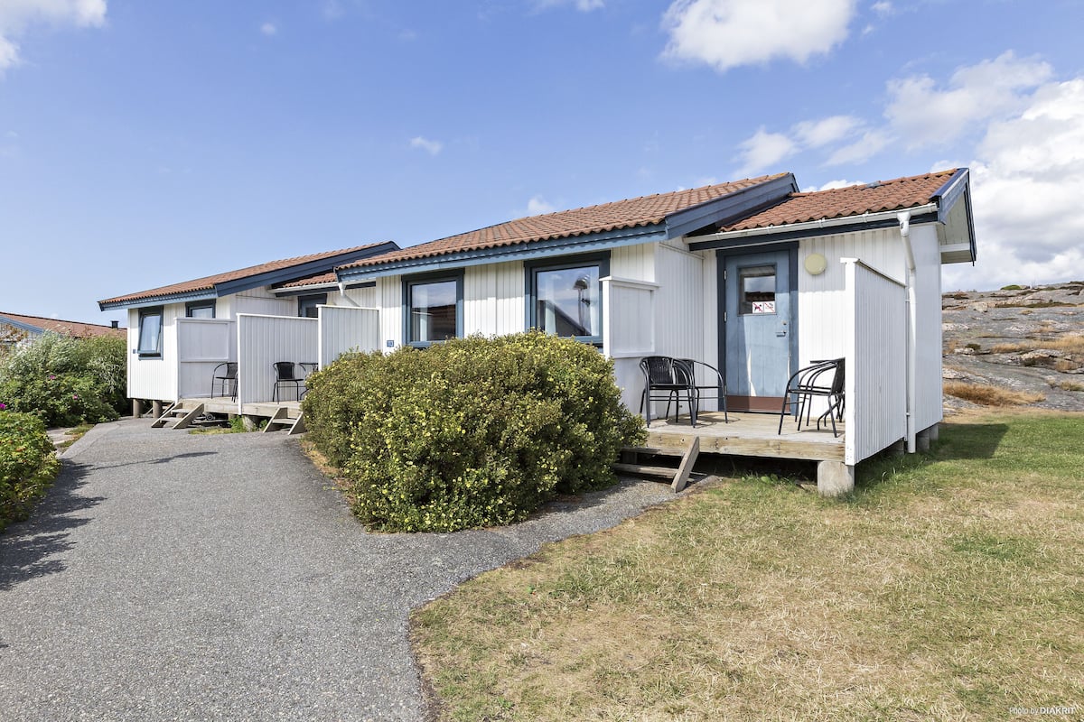 A row of mobile homes with a gravel path leading to the entrance, surrounded by greenery.