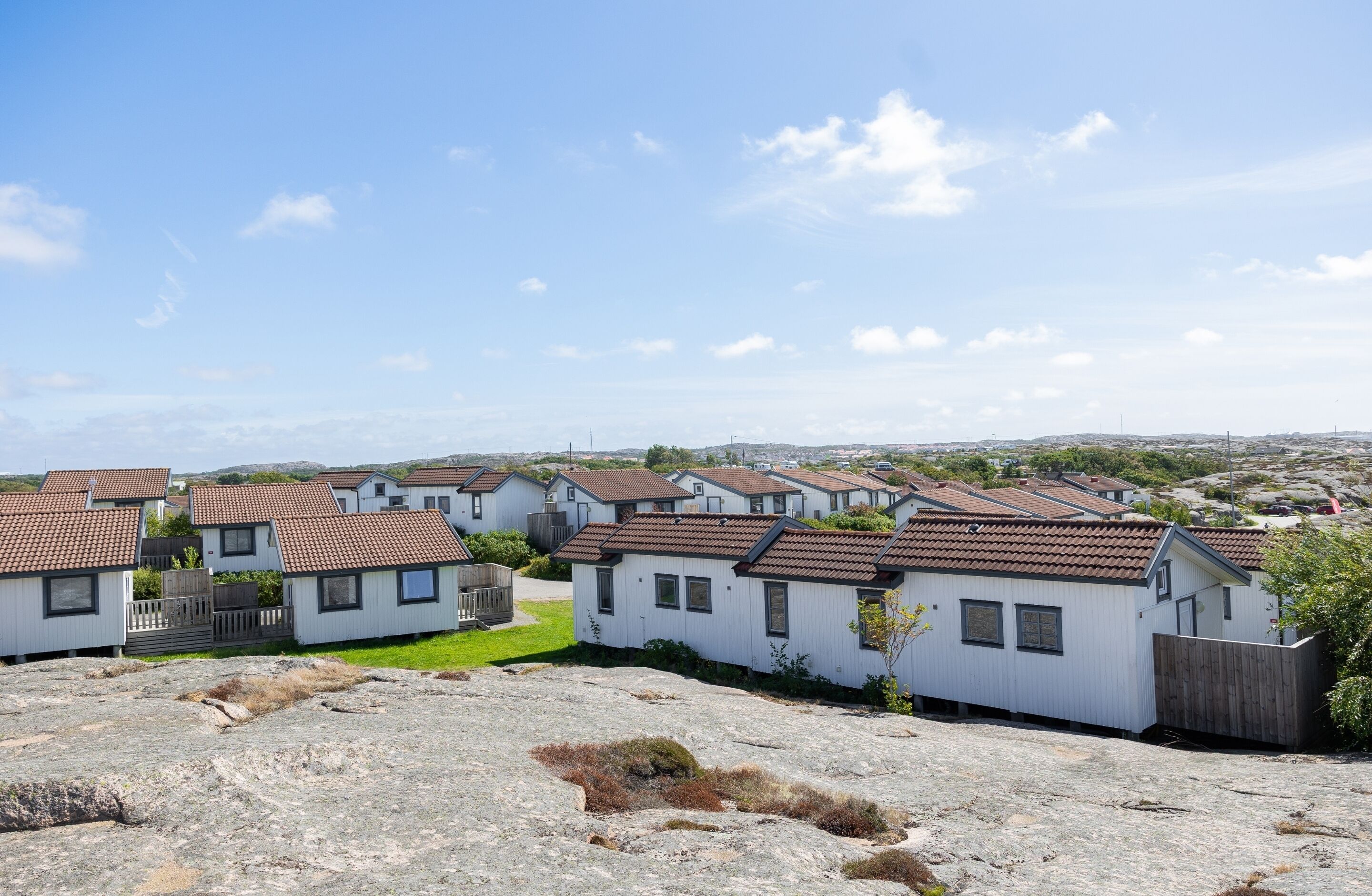 A row of white mobile homes with brown roofs, set against a clear sky.