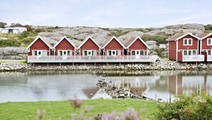 A row of red wooden cabins with white railings, situated by a calm lake with a rocky shoreline.