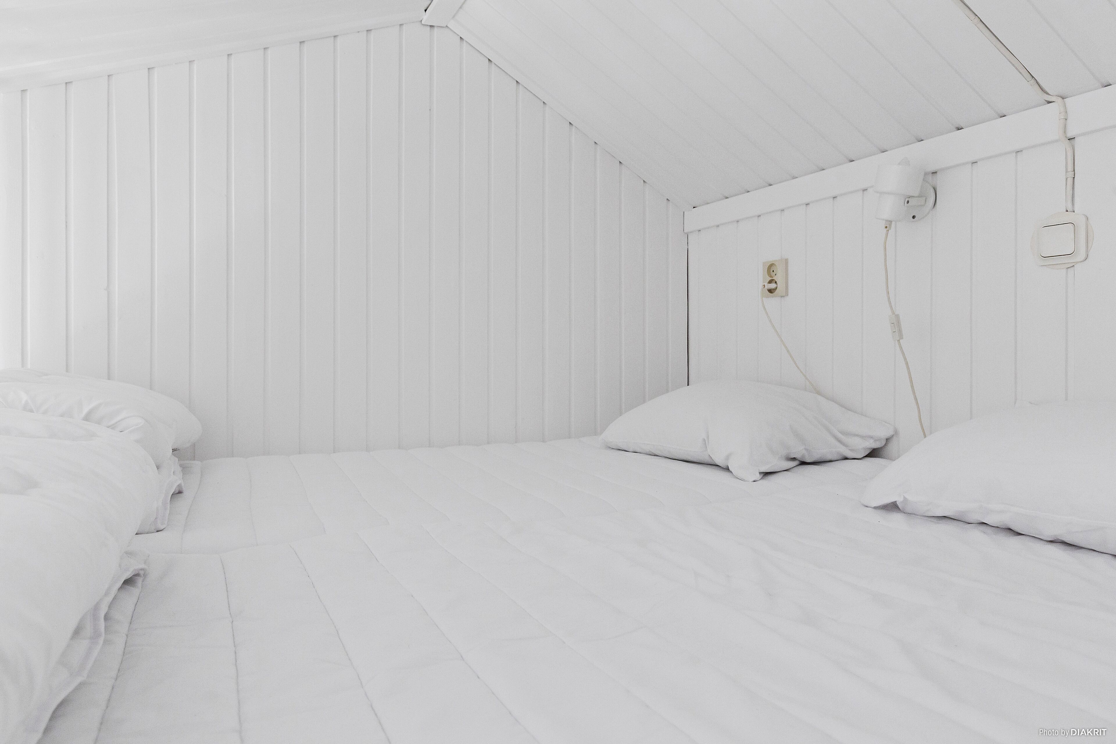 A white room with two beds, each with white bedding and pillows.