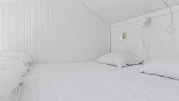 A white room with two beds, each with white bedding and pillows.