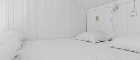 Ein helles Zimmer mit zwei Betten, jeweils mit weißer Bettwäsche und Kissen.