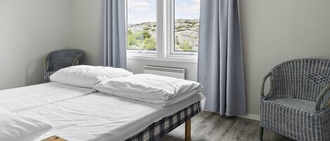 A bedroom with a bed, a chair, a window with curtains, and a view of the outdoors.
