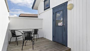 A wooden deck with a table and chairs, a blue door, and a white building with a tiled roof.