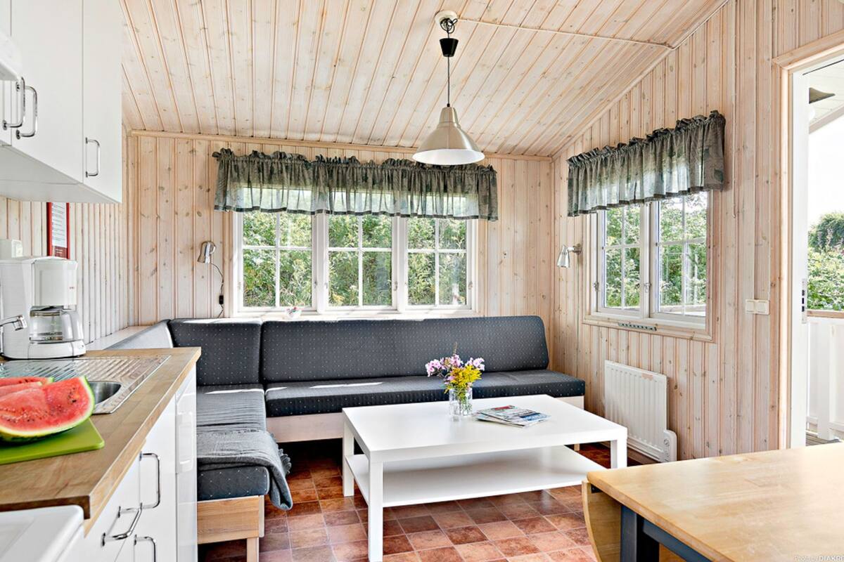 Una habitación acogedora de estilo cabaña con interior de madera, kitchenette, zona de comedor y ventanas amplias con vistas al entorno natural.