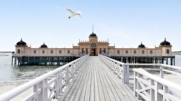 A wooden pier leading to a building with domed towers and a central clock tower.