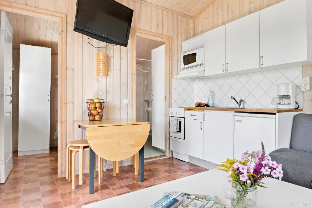 A compact kitchen with a microwave, oven, and sink, a dining area with a table and chairs, and a television mounted on the wall.