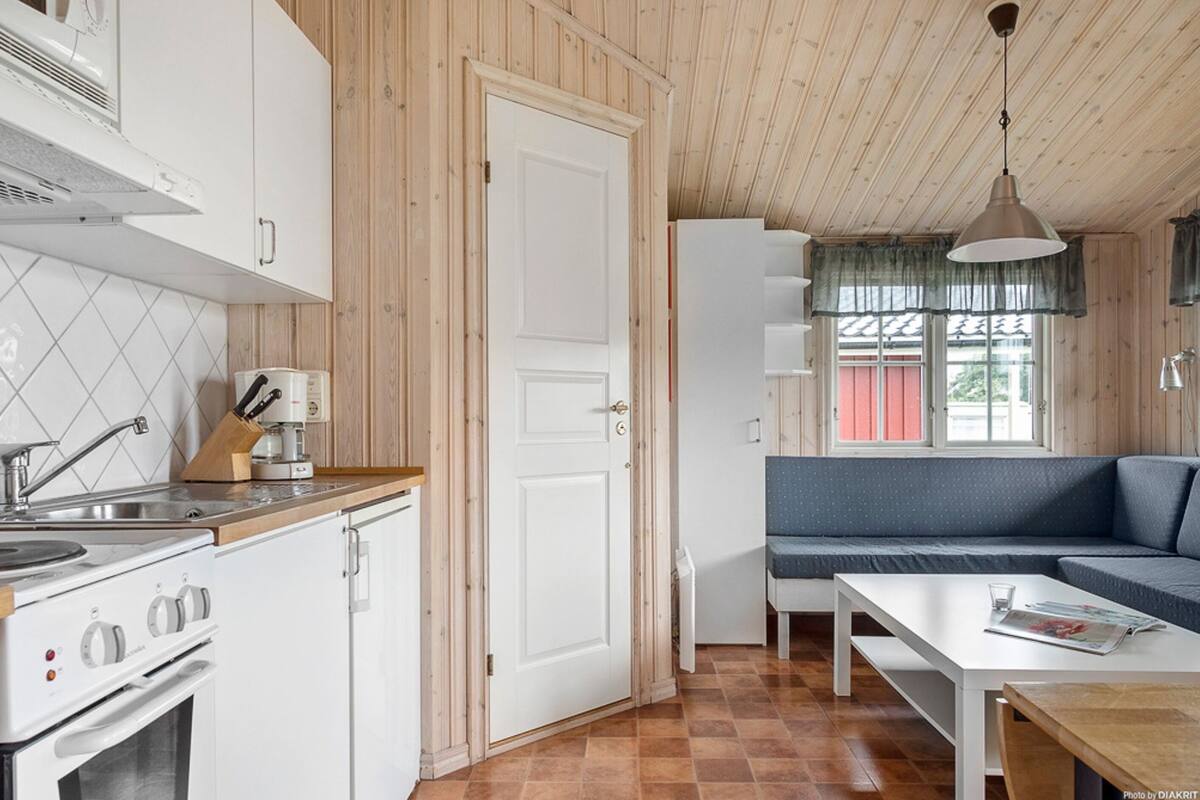 Una cocina con armarios blancos, una estufa y un lavaplatos. Hay una zona de comedor con una mesa y un sofá azul.