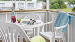 A white plastic chair with a blue towel draped over it, a white plastic table with a newspaper, and a bottle of water and a glass on the table. - First Camp Kärradal (Varberg)