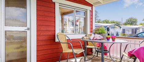 A red building with a covered patio area featuring a table and chairs, a window, and a door.