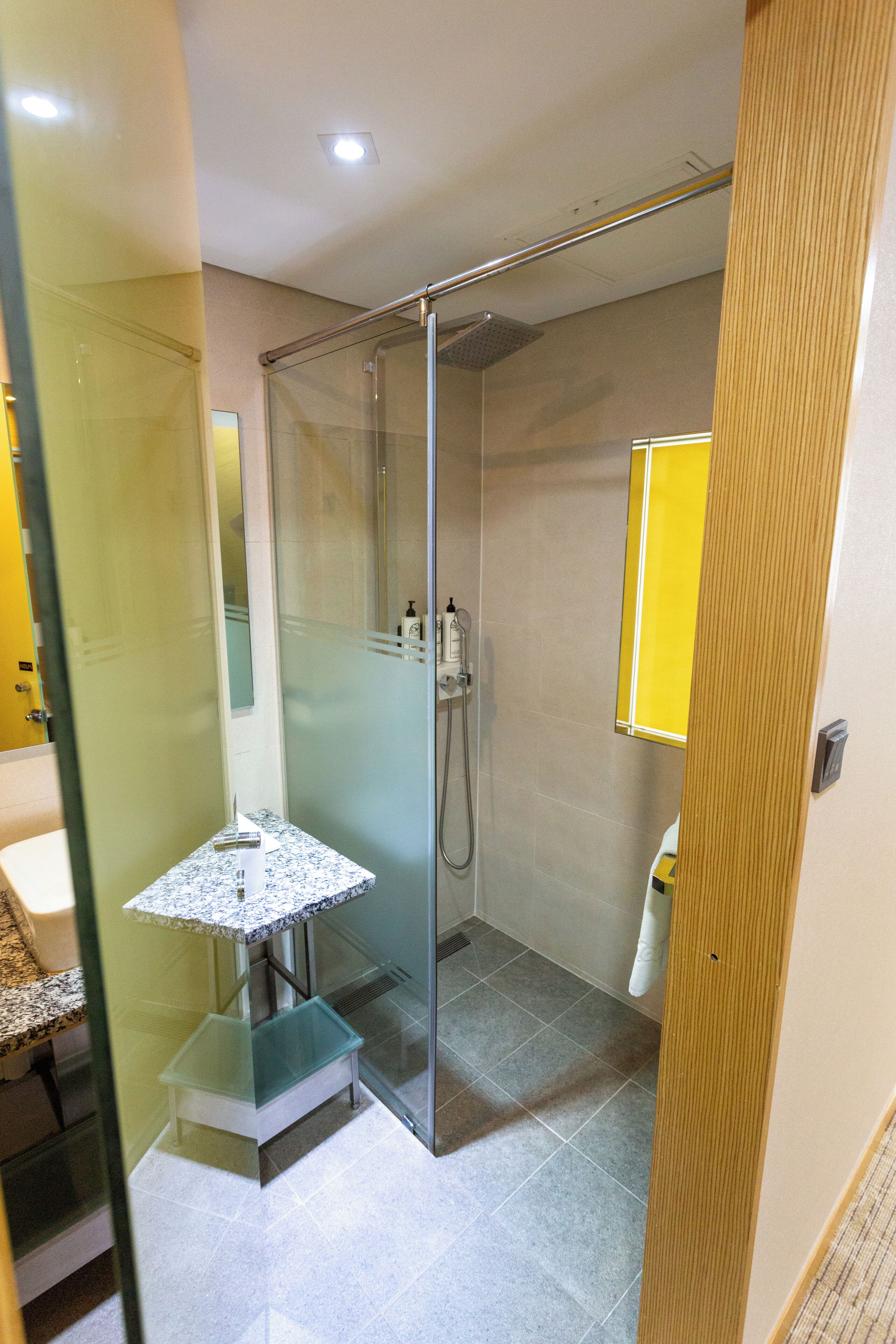 Un baño moderno con cabina de ducha de vidrio, tocador pequeño con encimera de mármol y espejo con marco amarillo.