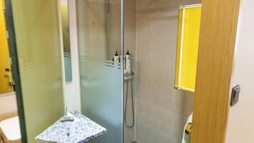 Un baño moderno con cabina de ducha de vidrio, tocador pequeño con encimera de mármol y espejo con marco amarillo.