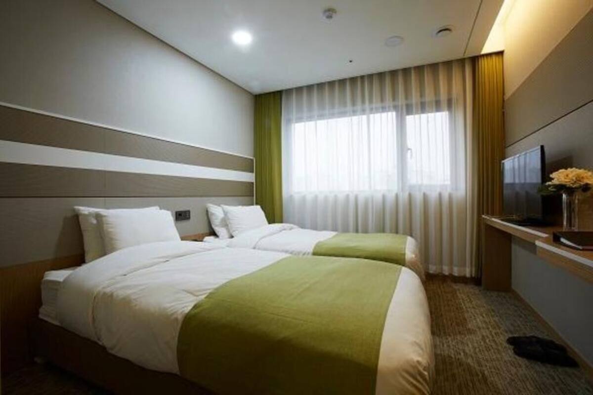 Une chambre d’hôtel avec deux lits, une télévision, une fenêtre avec des rideaux et un sol recouvert de moquette.