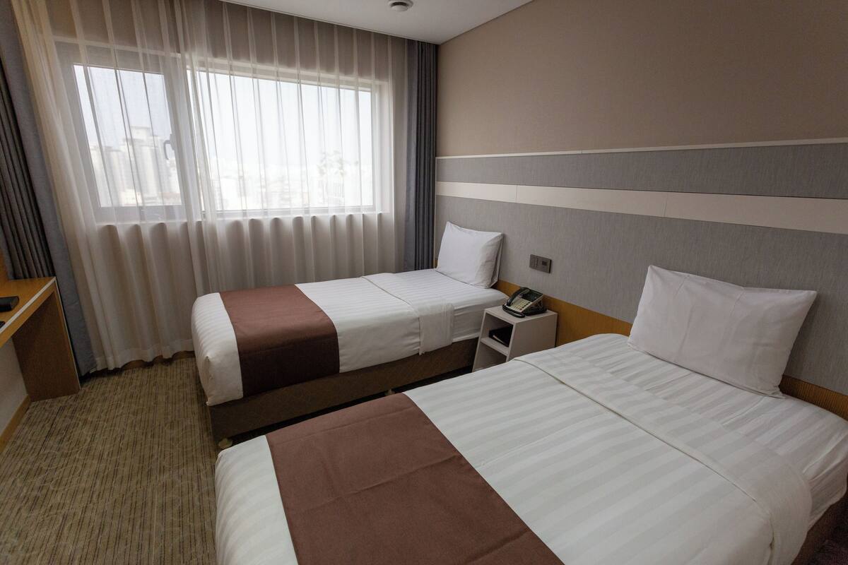 Une chambre d’hôtel avec deux lits, une table de chevet avec un téléphone et une fenêtre avec des rideaux.